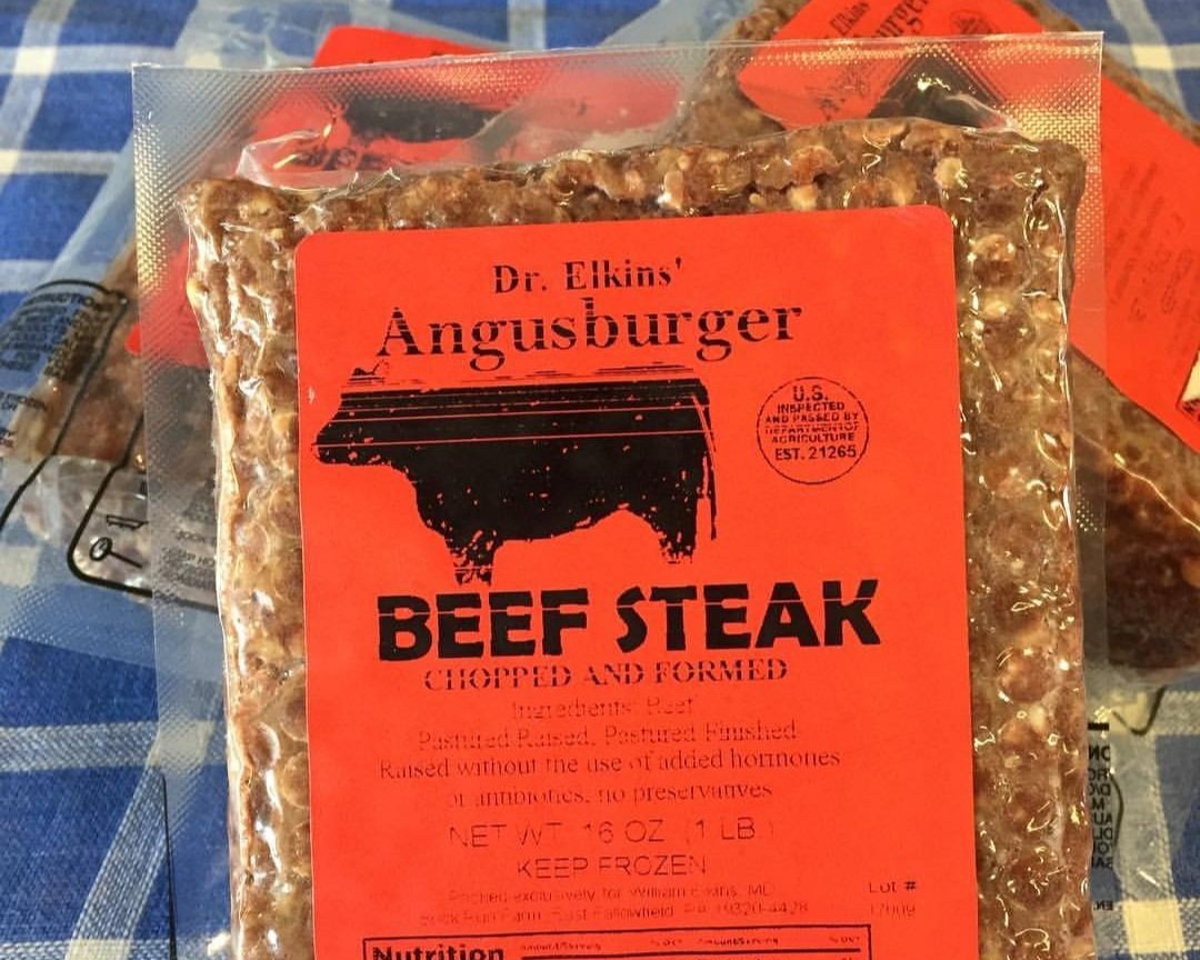 Packaging of Dr. Elkins' Angusburger beef steak, labeled "Chopped and Formed," featuring a bright orange design. The label highlights that the beef is pasture-raised, finished without added hormones, and contains no preservatives. The package weighs 16 ounces and includes storage instructions to keep frozen.